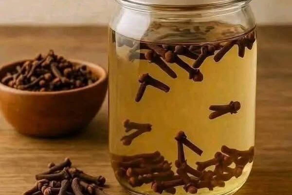 Whole cloves in a wooden bowl beside a jar of cloves steeping in water