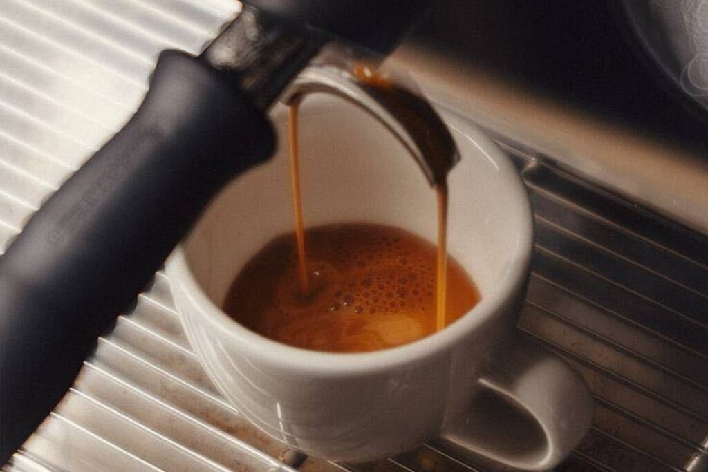 Fresh espresso pouring from a portafilter into a small white cup